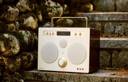 Bærbar cremefarvet højttaler, metalgitter, to højttalere, diskant, stor central knap, Bluetooth-skærm, forfra set