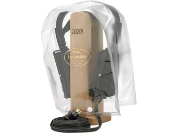 Custodia protettiva STAX CPC-1 in plastica trasparente flessibile, vista frontale, forma a campana con due bottoni a pressione bianchi alla base e logo dorato centrale che lascia intravedere il supporto per cuffie in legno chiaro e le cuffie nere all’interno