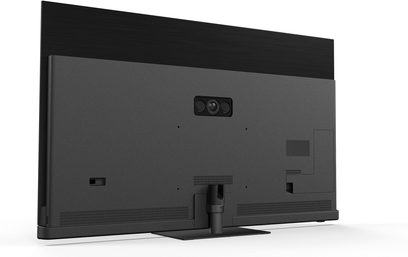Mattmust Panasonic TV-77Z90B kõrglahutusega teler, mille ülaosa on harjatud musta viimistlusega, tagakülg tekstureeritud plastist, integreeritud kolmeläätsekaameramooduliga ning silindrilisel metalljalal ristkülikukujulise alusega, tagantvaade kergelt nurga alt