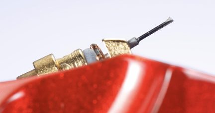 Primeiro plano oblíquo de um minúsculo conjunto em metal dourado e plástico preto emergindo de uma caixa vermelha com glitter