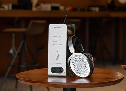 Amplificador/DAC para auriculares en aluminio plateado, vista en tres cuartos, rueda y conexiones XLR y jack de 6,35 mm, auriculares con rejillas