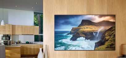 Samsung QE55Q70R-fladskærm, der viser et billede af et havlandskab med klipper og brusende bølger i et moderne, lyst træinteriør
