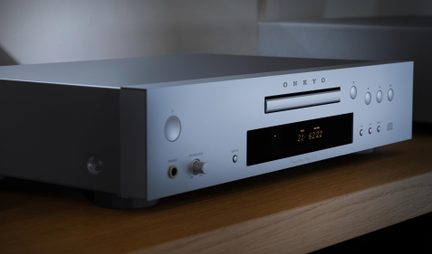 Stříbrný kovový CD přehrávač, štěrbinové vkládání, černý displej, sluchátkový výstup a tlačítka, pohled zleva zepředu v tříčtvrtečním úhlu