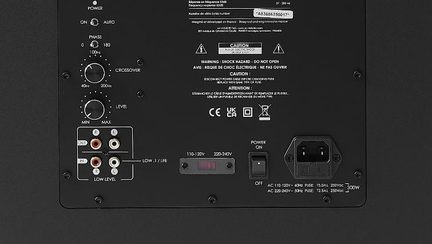 Černý kovový zadní panel basového reproduktoru, ovladače fáze/vypnutí/úrovně, vstupy RCA, IEC konektor