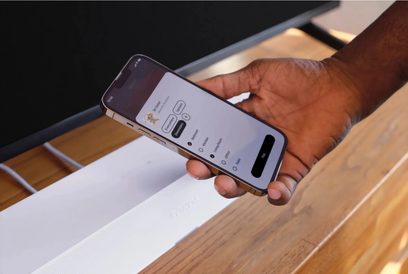 Nutitelefon, millel on Sonose rakendus avatud, käes hoituna puulaua kohal, lähinägemus küljelt