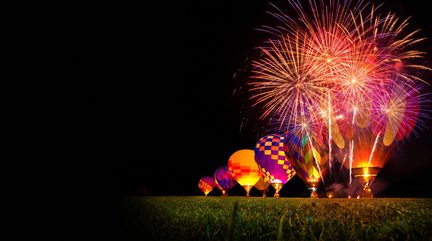 Mongolfiere colorate allineate di notte in un campo, illuminate da fuochi d'artificio multicolori