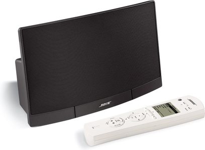 Kompakt rektangulær sort Bose RoomMate højttaler med frontgitter og hvid fjernbetjening, set forfra på hvid baggrund