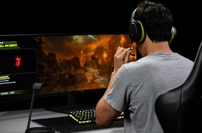 Audeze Penrose Xbox grønt hovedsæt på mands hoved, der spiller et krigsvideospil på computerskærm, set fra siden