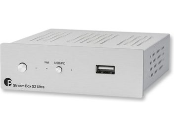 Stream Box S2 Ultra network audio player in silver, front view at a slightly oblique angle, rectangular casing with a metal front panel, circular button on the left, USB connector on the right, perforations on the top and sides.