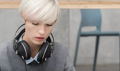 Ung kvinde med kort blondt hår, iført en grå sweater og med et sort hovedsæt på ørerne, med en eftertænksom mine