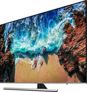 Samsung UE82NU8005-fjernsyn der viser et billede af en strand med turkisblå bølger, der bryder mod rødlige klipper