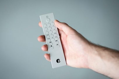 Sølvfarvet Pro-Ject-fjernbetjening holdt i hånden, set forfra med numerisk tastatur og afspilningsknapper