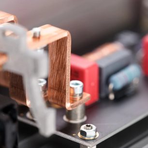 Tæt indre skråbillede af kobberstænger, metal skruer og møtrikker i sølvfarve, med røde og blå elektroniske komponenter monteret på printplade til Inakustik AC-3200 Filter Digital SCHUKO overspændingsbeskytter