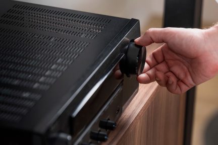 Juodas sukamasis rankenėlis ant šlifuoto metalo garso stiprintuvo su perforuota grotelių danga