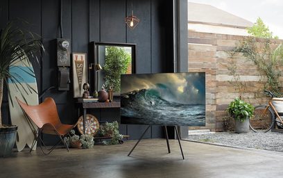 Samsung QE65Q7F 2018 fladskærms-TV, der viser en brydende bølge, på et stativ, i en moderne stue med cykel og planter
