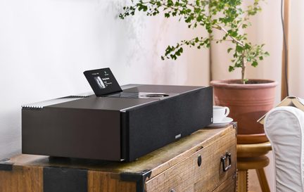 Svart ljudsystem med metallfinish, tyggrillar, uppfällbar skärm på ovansidan och vred, sned vy