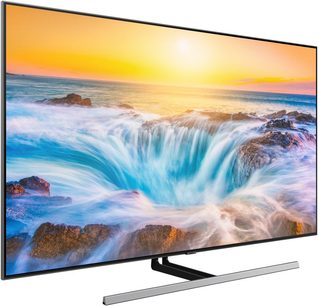 Samsung QE55Q85R fladskærms-TV, der viser et billede af bølger, der bryder over klipper ved solnedgang