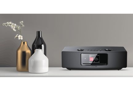 Guldfarvet vase, hvid vase, sort vase, sort radio med farveskærm, hvidt bord, grå væg