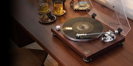 Giradischi in legno visto dall'alto con braccio di lettura argentato, disco nero, coperchio trasparente aperto, posizionato su un tavolo