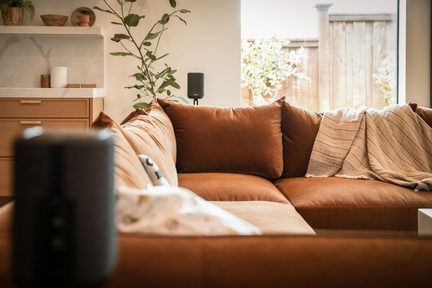 Črni brezžični zvočnik Sonos v moderni dnevni sobi z žametnim kavčem v karameli in bež plaidom