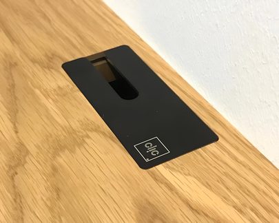 Lyst træbordplade med sort, rektangulær kabelgennemføring med aflange åbning, set ovenfra