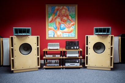 To lyse træhøjttalere flankerer et vintage hi-fi-møbel under et farverigt maleri af en kvinde med langt rødt hår