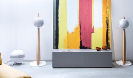 Coppia di diffusori hi-fi dal design bianco su supporti in legno in un salotto minimalista con un grande quadro astratto e colorato