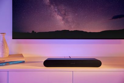 Sonos Ray svart lydplanke, sett forfra, plassert på et møbel foran en vegg med et bilde av en stjernenatt projisert