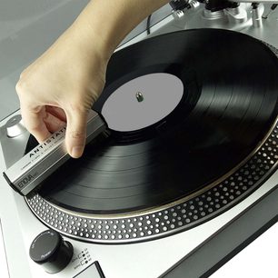 Pladespiller med sort tonarm, vinylplade og hånd, der holder en antistatisk Enova HIFI BVA 20 kulstofbørste
