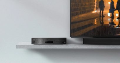 Panasonic SC-HTB700EGK sort soundbar, set forfra, placeret på en hvid hylde foran en tændt tv-skærm