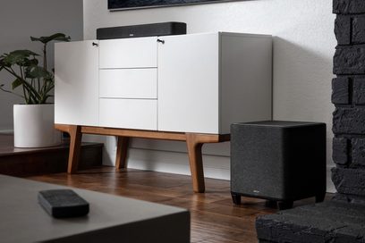 Denon Home Subwoofer svart, frontvy, placerad på golvet bredvid en vit möbel med lådor