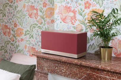 Triangle AIO 3 connected wireless speaker in red ochre, front view on marble table in front of floral patterned wall