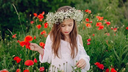 Ung pige med en krans af hvide blomster i en mark med røde valmuer, der kigger ned
