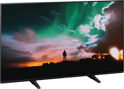 Panasonic TX-48JZ980E-fjernsyn, der viser en menneskelig silhuet foran en grøn og orange himmel med hvide skyer