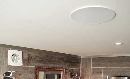 Altoparlante da soffitto rotondo bianco incassato in un bagno moderno con piastrelle effetto legno e faretti LED