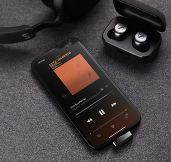 Безжични слушалки Sennheiser в отворен калъф до смартфон, който възпроизвежда джаз албум, върху сива материя