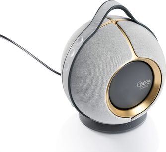 Devialet Mania Opéra de Paris Bluetooth-högtalare i ljusgrå och guldton, sedd framifrån med en lätt lutning, grå tygkåpa