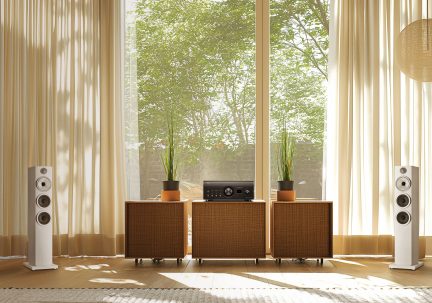 Foran, 2 hvite høyttalere, 3 tremøbler, 3 potteplanter, svart forsterker, beige gardiner, stort vindu