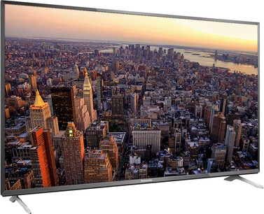 Panasonic TX-50CX700E teler, mis näitab tihedalt asustatud linna õhuvaate paljude pilvelõhkujatega päikeseloojangul