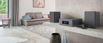 Denon RCD-N10 hvidt "alt-i-ét" hi-fi-system i en stue med grå sofa, puder og sofabord