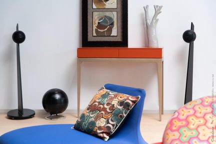 Sorte hi-fi-højttalere på standere i en moderne stue med sfærisk subwoofer og orange konsol