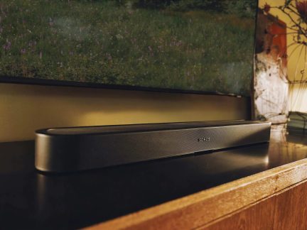 Soundbar Sonos nera posizionata su un mobile sotto un televisore che mostra un prato fiorito