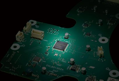 Placă electronică verde în prim-plan, cu microcontroler central iluminat, condensatori și conectori bej din plastic