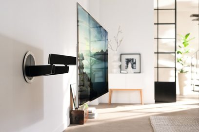 Zwarte wandgemonteerde TV-standaard, bevestigd aan de witte muur van een moderne woonkamer, met een platte beeldscherm waarop een vage natuurlijke landschap wordt weergegeven