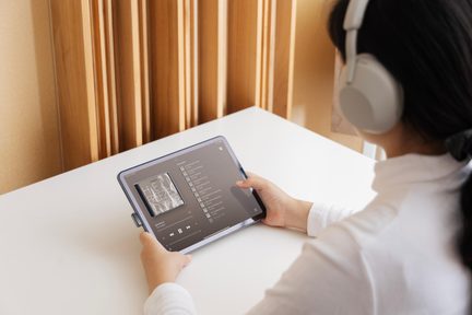 Cuffie wireless grigie su donna che utilizza un tablet touchscreen per ascoltare una playlist musicale