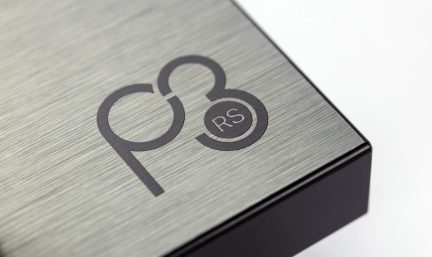 Superfície metálica escovada com inscrição preta "p3 RS", borda inferior preta, ângulo de visão em close-up.