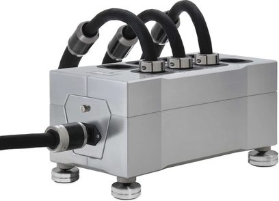 Furutech NCF Power Vault strømforsyningsstikdåse i børstet sølvaluminium, set fra trekvart forfra, placeret på fire cylindriske fødder, med øvre udgange omkranset af metalringe, der holder fletede sorte kabler, og en IEC-stikforbindelse tilsluttet forsiden