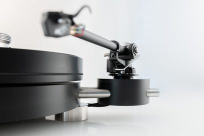 Vista lateral cercana del tocadiscos hi-fi Transrotor Max Nero RB330 negro, de aluminio anodizado, que muestra el plato cilíndrico liso, el brazo de lectura negro RB330 y el soporte tubular de acero cepillado