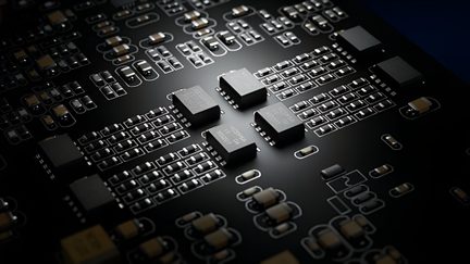 Carte électronique noire en résine époxy, vue en gros plan oblique, comportant plusieurs microcircuits carrés en plastique noir et de nombreux composants CMS beige et argentés