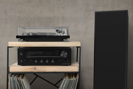 Črni vinilni gramofon s prozornim pokrovom, črni ojačevalnik, lesena polica, črni zvočnik, vinilne plošče